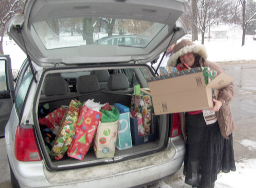 MAKING A DIFFERENCE — Vicky Stockton Allen, vice president of Alpha Chi, peeks from under her coat hood as she places the many gifts from Alpha Chi members into her car for distribution during one of several community projects performed by the organization and its members.
 (Photo submitted)