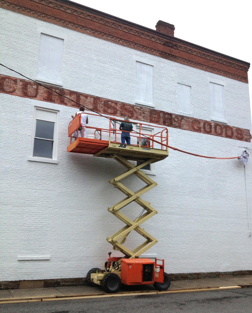 MEN AT WORK — Two workers on a scaffold paint the wall of the Camden VFW post white to give artist Jane Grace Taylor a clean canvass to work on to paint the Camden Continentals Fife and Drum Corps mural.
