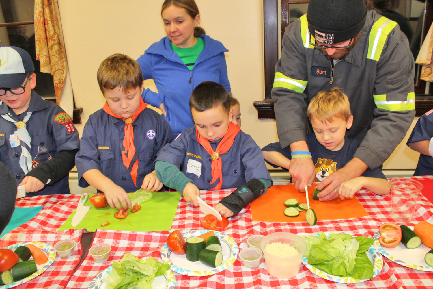SLICE AND DICE — Troops from Boy Scout Pack 50 of Rome, assisted by a couple parents, learn the proper and safe way to slice vegetables as they prepare hummus wraps with members of the Hamilton College Bon Appetit team.