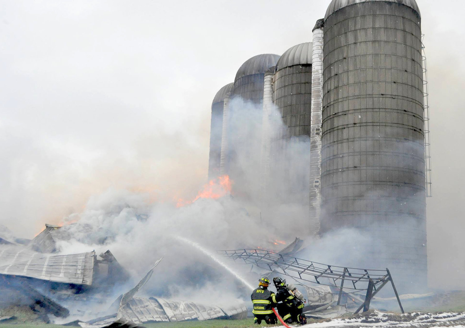 BARN DESTROYED —Local firefighters spray down a smoldering tin roof after a 60-foot by 200-foot cow barn was destroyed by fire on Whittaker Road in Trenton on Sunday. Fire officials said 250 head of cattle were killed in the blaze.