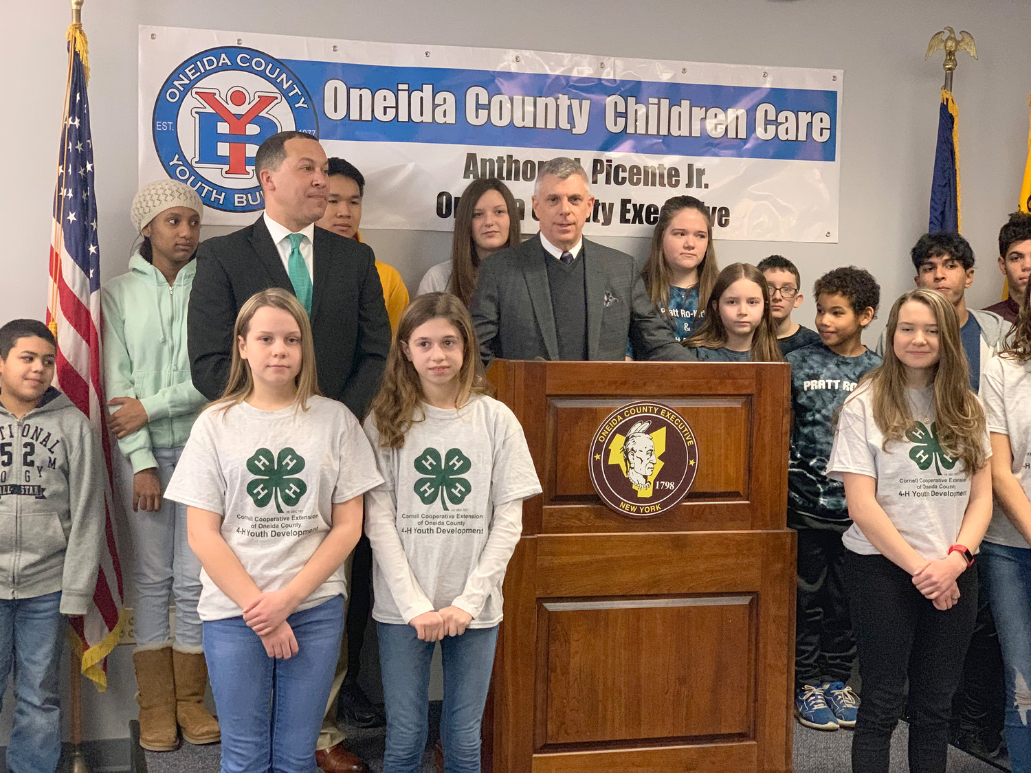 VOLUNTEER EDUCATION — Oneida County Youth Bureau Director Kevin Green and Oneida County Executive Anthony J. Picente Jr., at lectern, pose at the county office building in Utica Wednesday with youth volunteers during a commemoration of 10 years of Oneida County Children Care, an initiative to link youth volunteers with service agencies in need of volunteers.
