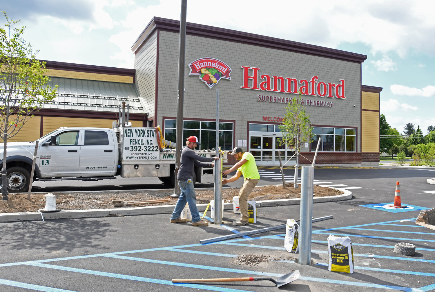 FINISHING TOUCHES — A crew from New York Fence, of Rochester, install posts in the parking lot of the new Hannaford supermarket at the corner of Turin and Chestnut streets this  morning. The store is gearing up for a Friday, June 20, opening.