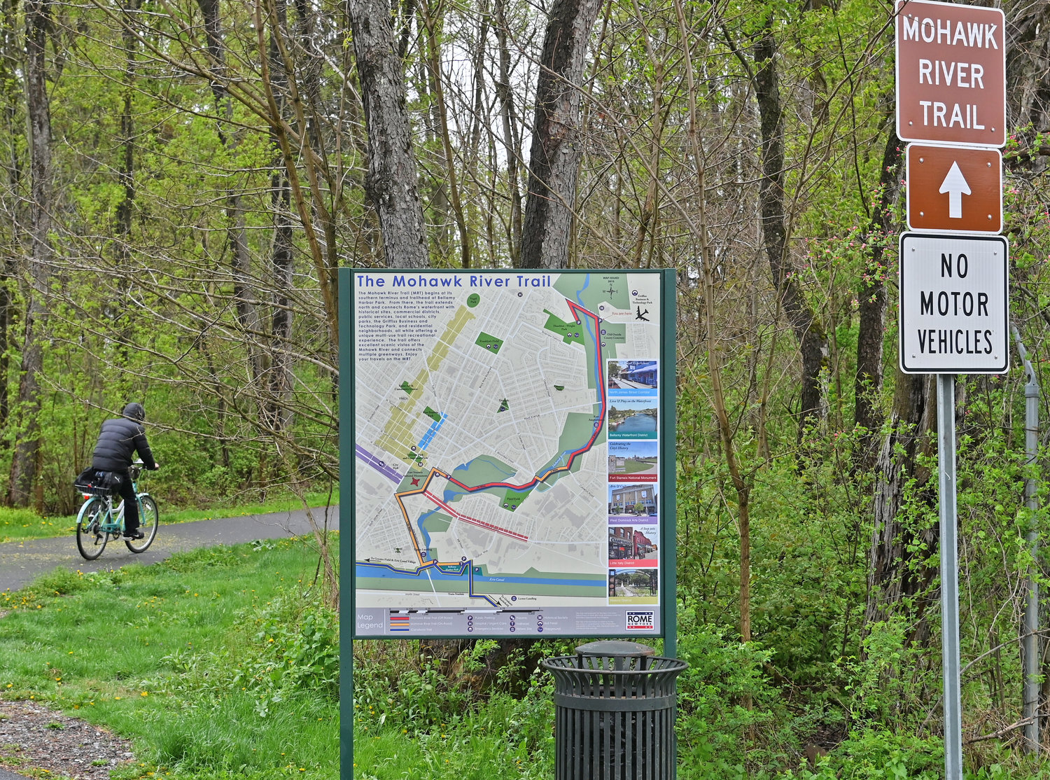 INTO THE WOODS — A bicyclist braves the rain as they head southwest at the Mohawk River Trialhead on East Chestnut Street on Tuesday. The city is moving forward with Phase II of the trail plan, which would begin construction of the trail north to Ridge  Mills from the trailhead to a spot near the intersection of Black River Boulevard and Wright Settlement Road.