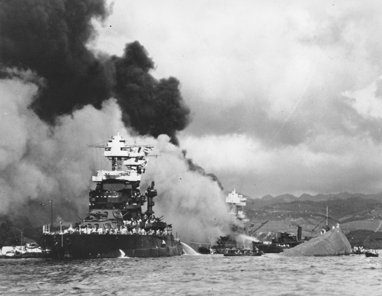 FILE - In this Dec. 7, 1941, file photo, part of the hull of the capsized USS Oklahoma is seen at right as the battleship USS West Virginia, center, begins to sink after suffering heavy damage, while the USS Maryland, left, is still afloat in Pearl Harbor, Oahu, Hawaii. Pearl Harbor survivors and World War II veterans are gathering in Hawaii this week to remember those killed in the Dec. 7, 1941 attack. Those attending will observe a moment of silence at 7:55 a.m., the minute the bombing began. The ceremony will mark the 80th anniversary of the attack that launched the U.S. into World War II.
