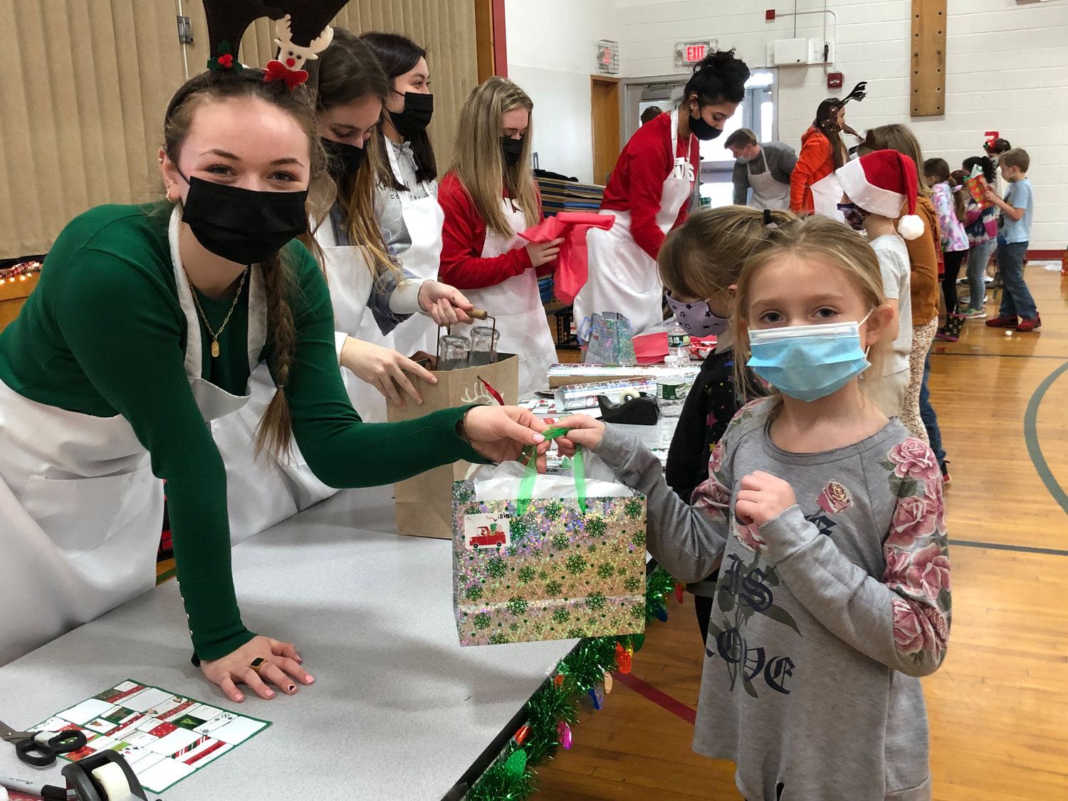 IT’S A WRAP — Haylee Moore, left, a Vernon-Verona-Sherrill High School Honor Society student, helps second-grader Lillian Sellnow wrap a gift that the youngster selected to give a loved one from Santa’s Workshop at the J.D. George Elementary School.