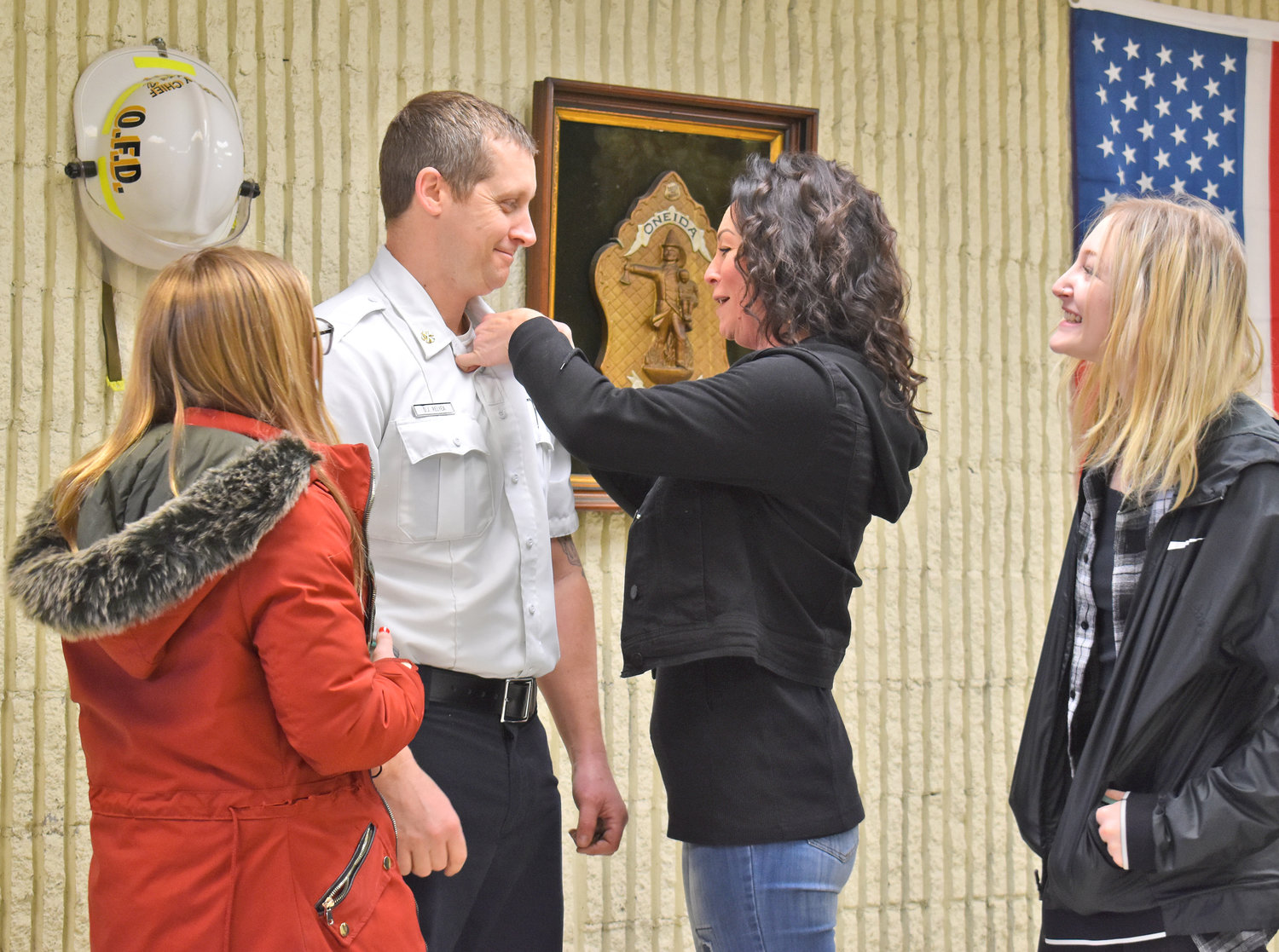 SWORN IN — Dennis Relyea smiles as his wife, Kendra, affixes a collar pin signifying Relyea’s new rank in the Oneida Fire Department. Relyea, a 12-year member of the department, was appointed as deputy chief. He had previously held the rank of lieutenant. Looking on are the couple’s daughters, Natalie, left, and Kayla Rose-Richmond, right.