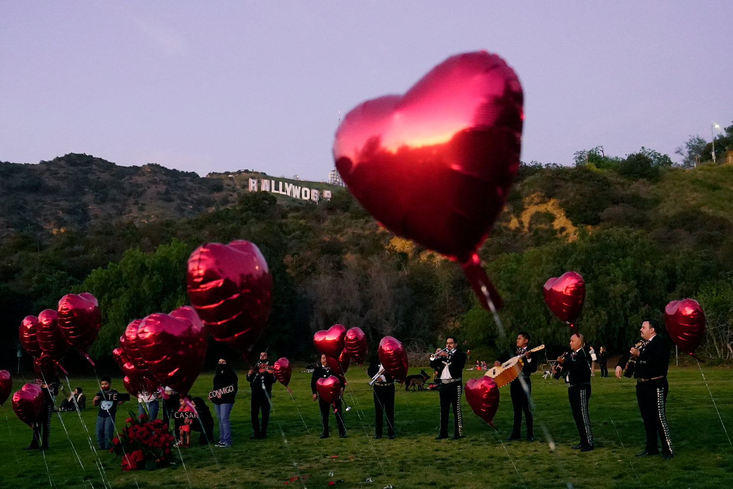 FILE - A Mexican Mariachi band surrounded by heart-shaped balloons awaits the arrival of a couple's wedding proposal ceremony at the Lake Hollywood Park in Los Angeles, on Valentine's Day, Monday, Feb. 14, 2022. Attending weddings can be expensive, between travel and lodging, gifts and extra events like bachelor and bachelorette parties. So plan ahead for these expenses, particularly as wedding season approaches and celebrations that were postponed or rescheduled reappear on your calendar.   (AP Photo/Damian Dovarganes, File)