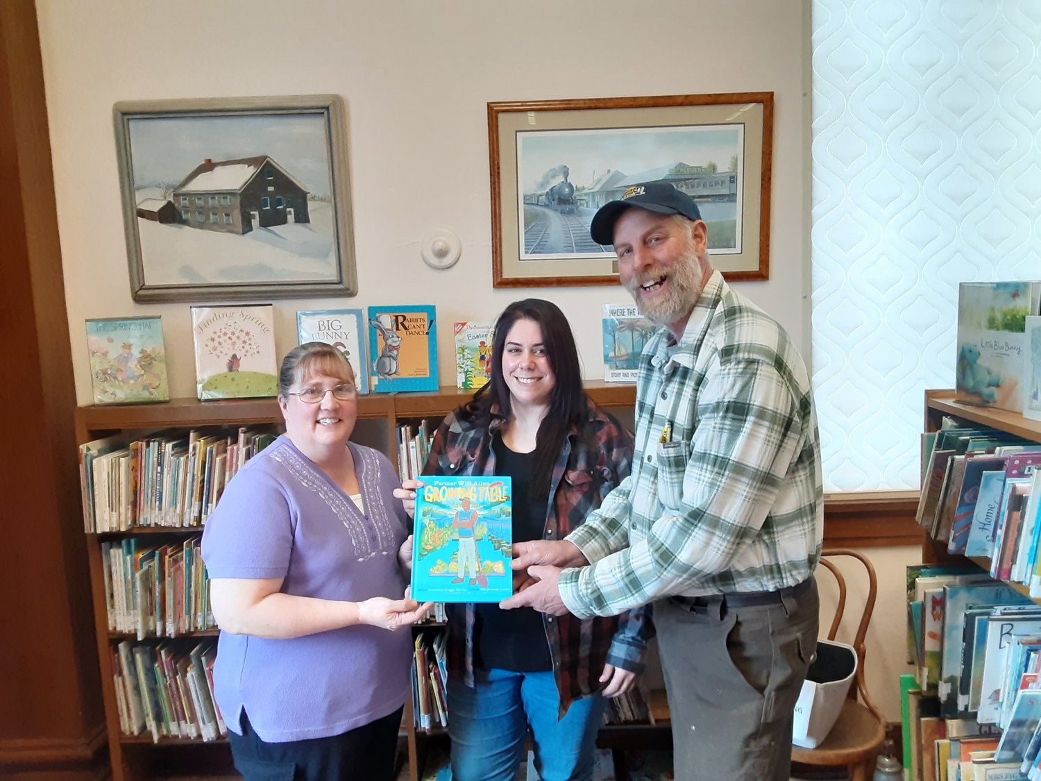 DONATION — This year’s New York State Agricultural Literacy Week book "Will Allen and the Growing Table" is presented to Lorraine Hefner and Megan Goldstein, co-librarians at Didymas Thomas Library, in Remsen, by Benjamin Simons, of the Oneida County Farm Bureau.