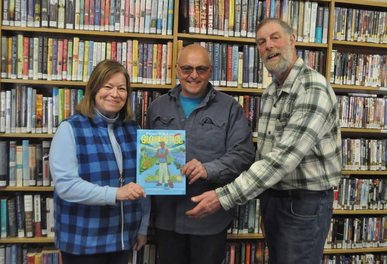 GROWING IN POPULARITY — Agricultural Literacy Week book selection "Will Allen and the Growing Table" is presented to Cindy McVoy, Holland Patent Librarian, left,  by New York Farm Bureau President David Fisher, center, along with Oneida County Farm Bureau member Benjamin Simons.