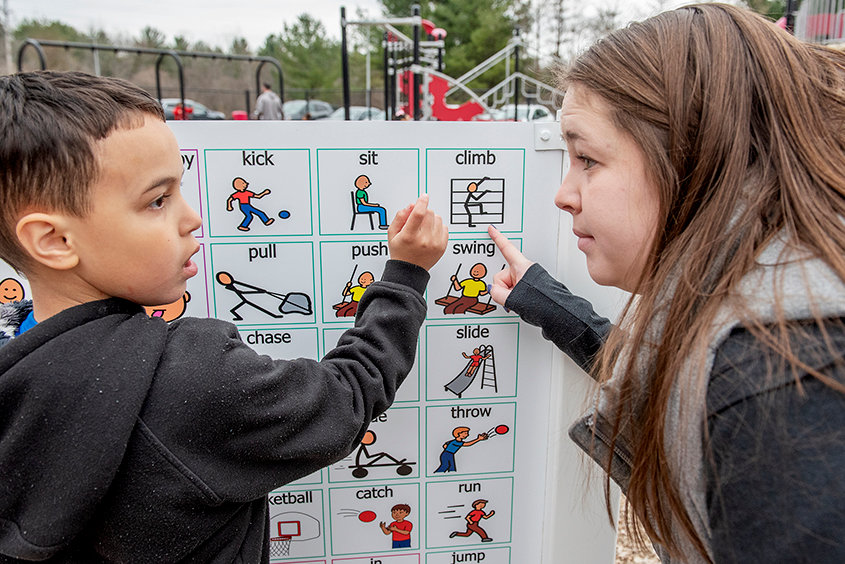 LET’S DO THIS — Jomar Rodriguez, 7, points to “climb” on the communication board with his K-2 Autism special education teacher Marisa White at Marie Curie Elementary in Amsterdam last week. A new communication board was installed inside the playground area to assist students with with special needs be better able to express what they would like to do during recess.