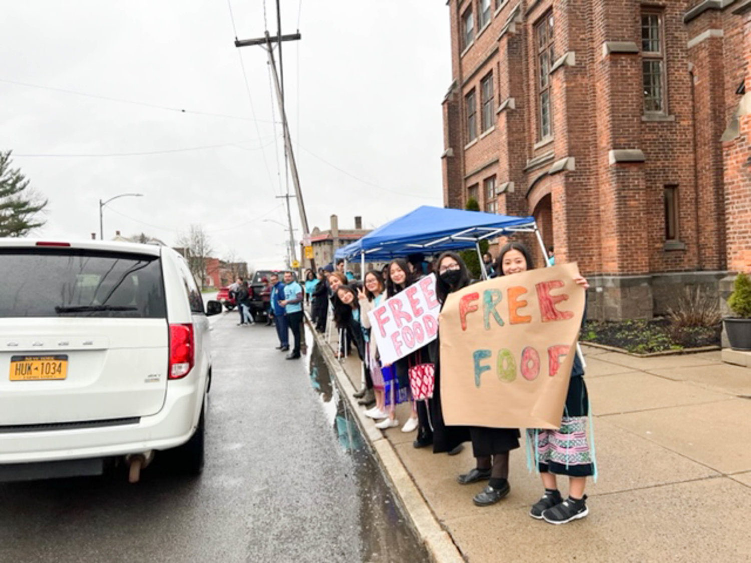 HELP FOR HUNGRY — Four of the Seventh-Day Adventist Churches in Utica gave away 203 baskets of food and toiletries to families in need, according to event organizers. Above, volunteers stand outside in the rain waiting to help load up arriving residents.