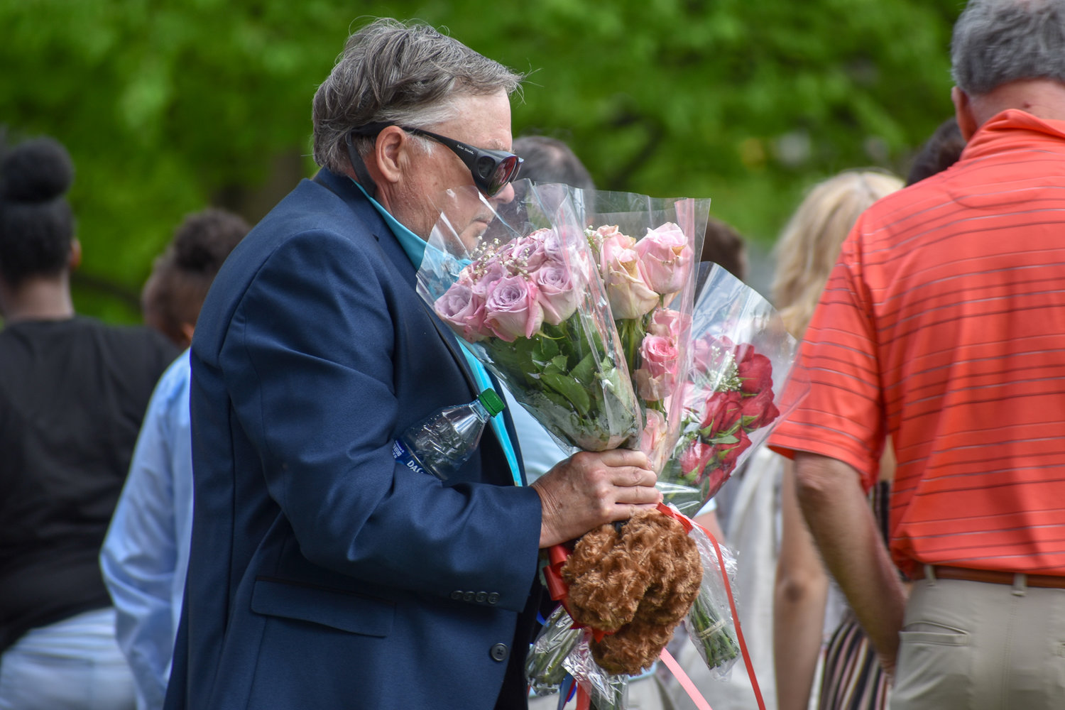A graduation guest finds his seat with celebratory flowers in tow.