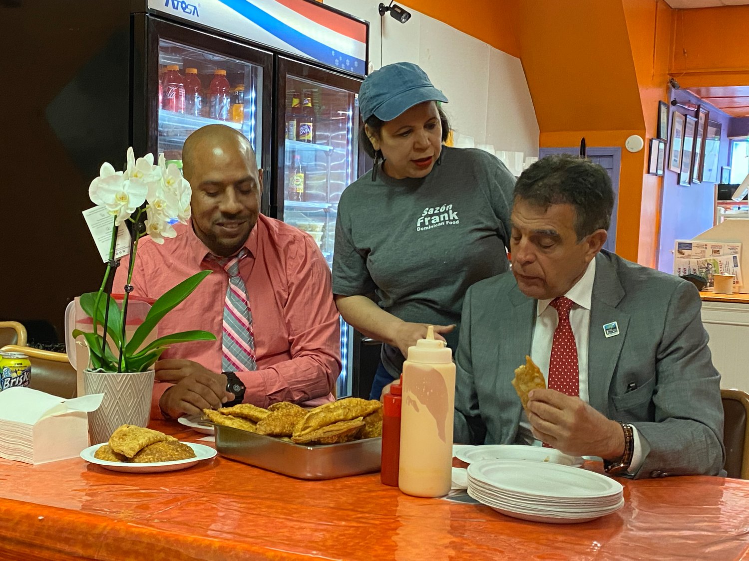 Nieve Nunez (center) checking in on Utica Mayor Robert Palmieri (right) as he enjoys an empanada from Sazón Frank Restaurant.