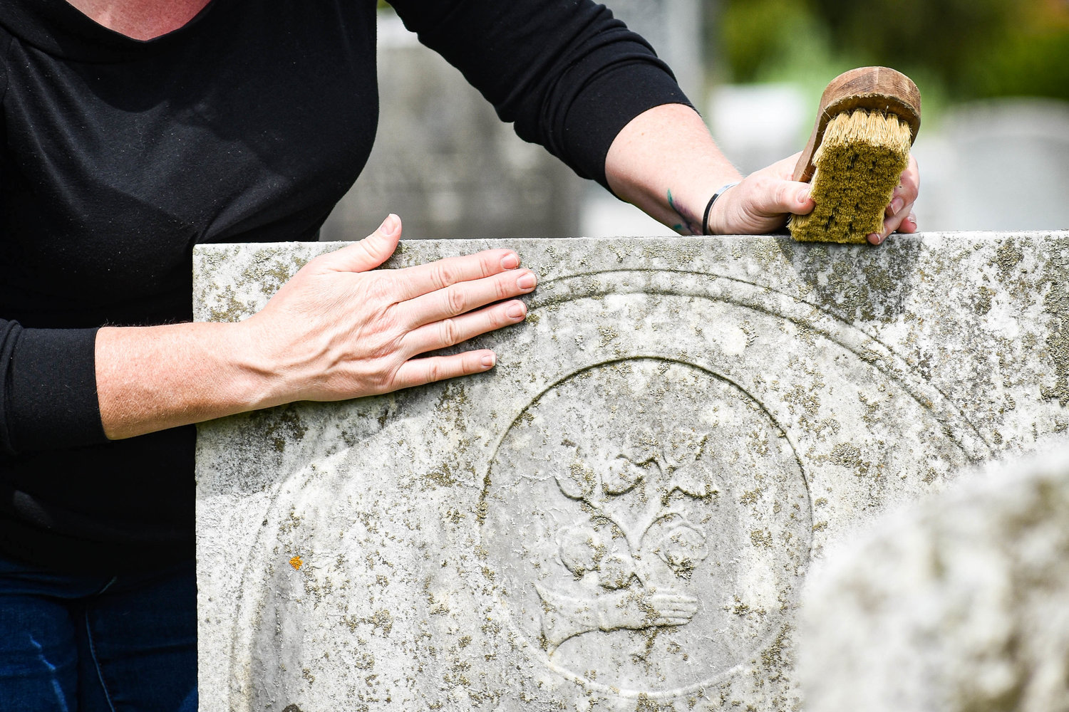 Megan Barnes inspects a gravestone that has not yet been cleaned at Madison Village Cemetery. The local earth science teacher has gained over 350k followers on TikTok by posting videos of her cleaning gravestones and sharing the stories of the deceased.