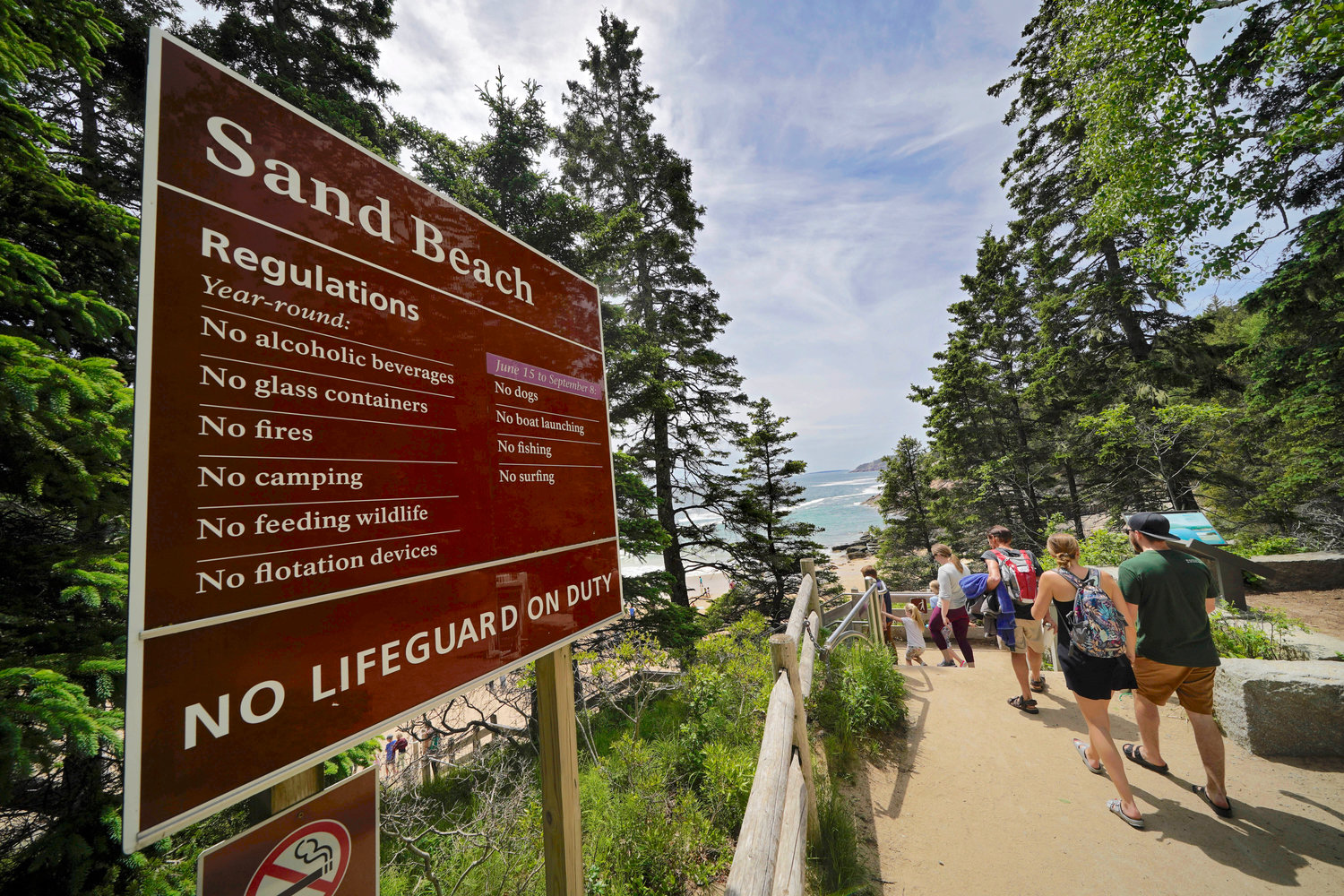 Beach-goers walk by a sign that warns of the absence of lifeguards at Sand Beach in Acadia National Park, Maine, on June 11.