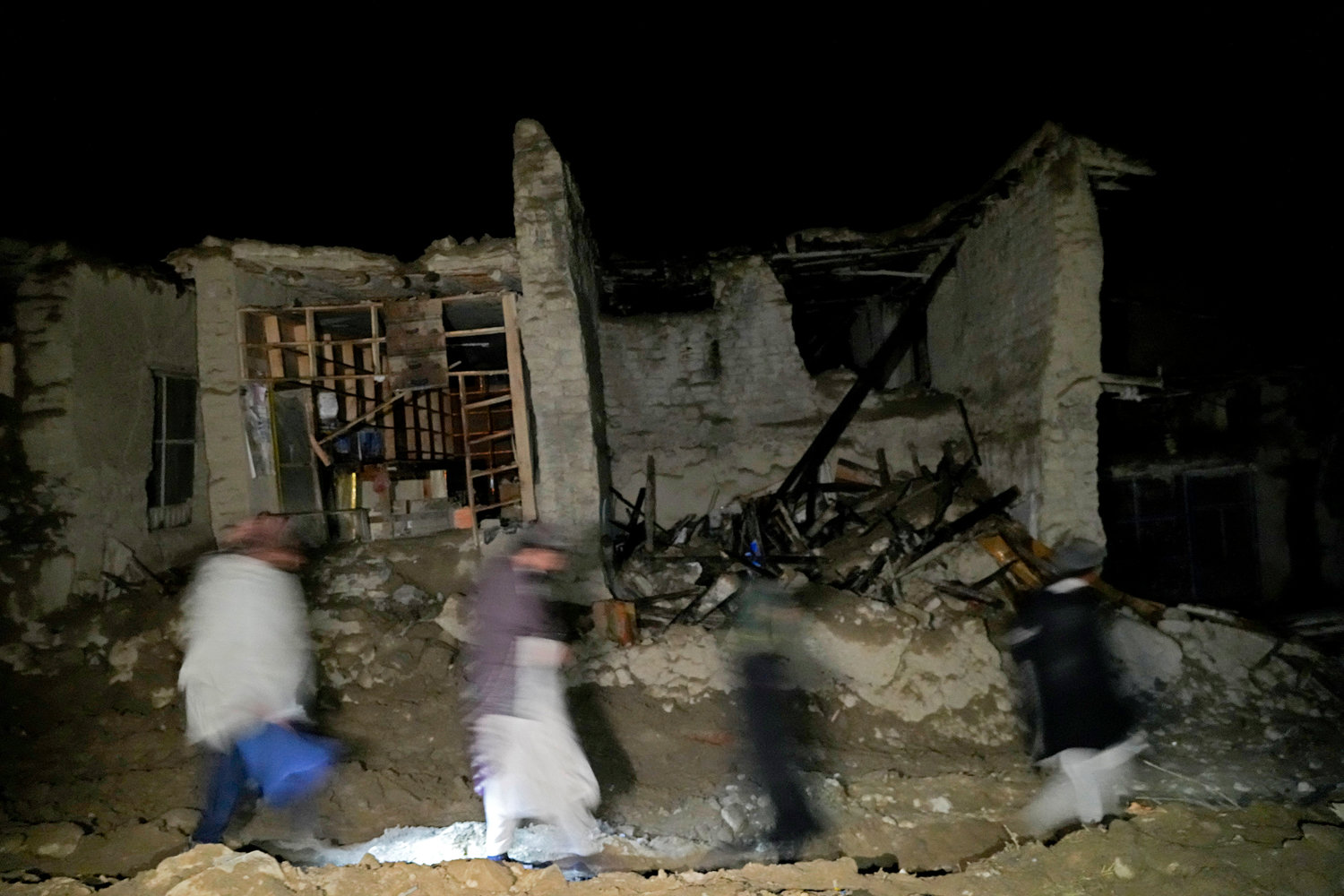 Afghans walk by a destroyed housein the village of Gyan, in Paktika province, Afghanistan, Wednesday, June 22, 2022. A powerful earthquake struck a rugged, mountainous region of eastern Afghanistan early Wednesday, flattening stone and mud-brick homes in the country's deadliest quake in two decades, the state-run news agency reported. (AP Photo/Ebrahim Nooroozi)