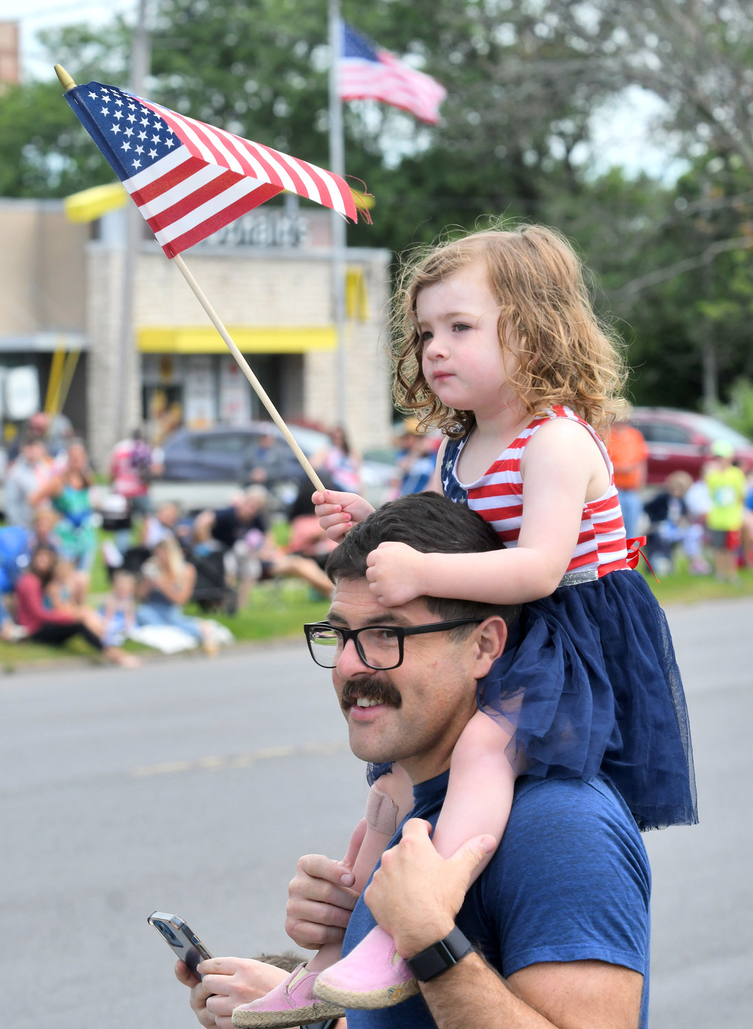 Lilia McMyler, 2, sits on the shoulders of her dad, William McMyler, as the  Fourth of July parade — featuring dozens of local groups and organizations — approaches them on Genesee Street in Utica.