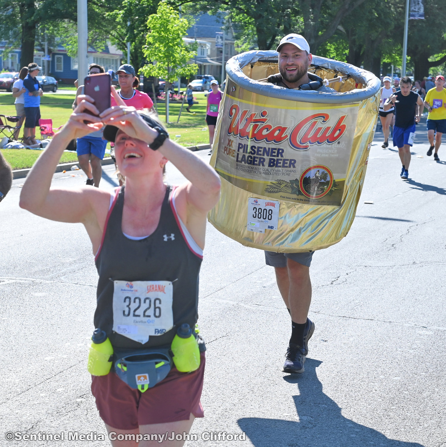 15k runner Lesley Allison of Lancaster, Mass., shoots a selfie with a runner dressed in a Utica Club beer can outfit on Memorial Parkway during the 45th Boilermaker Road Race.