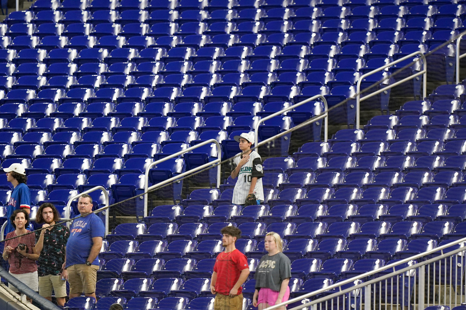 Baseball fans stand during the singing of the National Anthem before the start of a game between the Miami Marlins and the Texas Rangers, on Thursday in Miami. Major League Baseball teams head into the final months of the regular season struggling to fill the stands now, even without pandemic-related attendance restrictions.