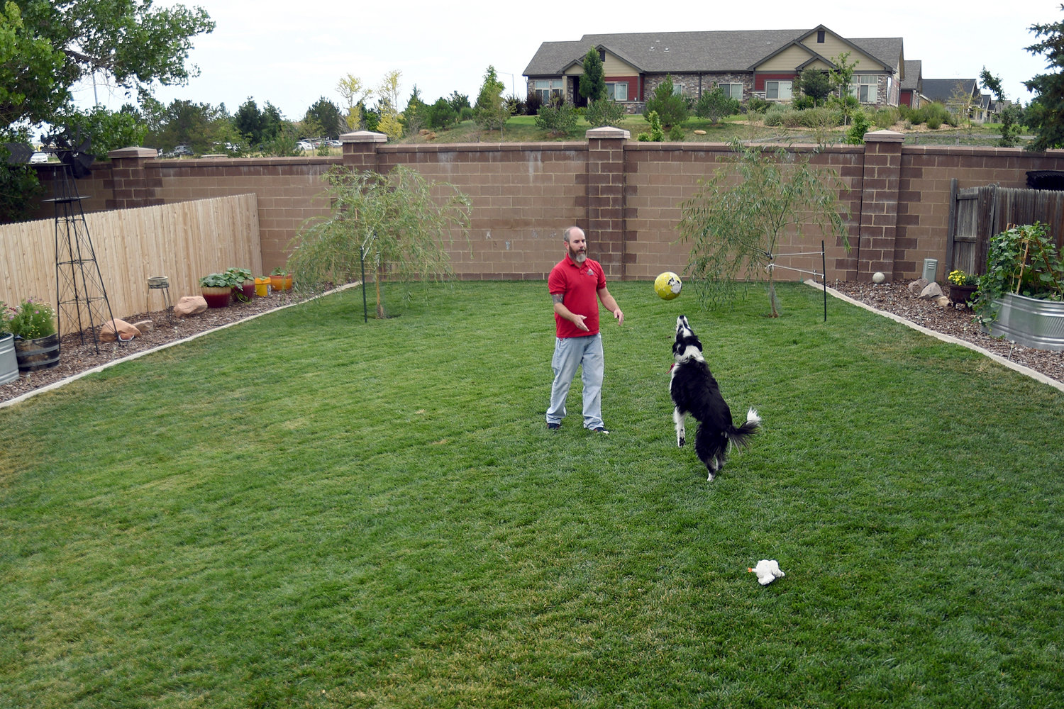 Kyle Tomcak plays with one of his dogs in the backyard of his house in Aurora, Colo., on Monday, July 18, 2022. Tomcak was in the market for a home priced around $450,000 for his in-laws and he and his wife bid on every house they toured, regardless of whether they fell in love with the home. He said his search became increasingly dispiriting as he not only lost out to investors fronting cash offers $100,000 over asking price but as mortgage rates started to balloon. He has since pulled out of the housing search. (AP Photo/Thomas Peipert)