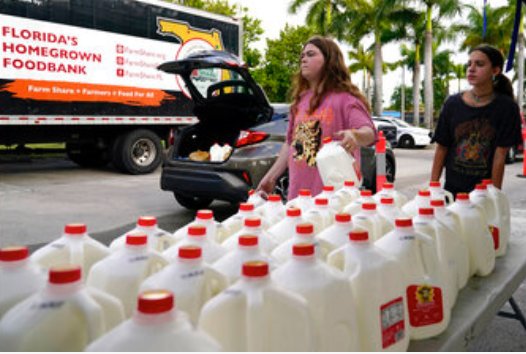 Vanessa Correa, left, and Gigi Fiske, right, pass out gallons of milk at a food distribution held by the Farm Share food bank in Miami recently. Long lines are back at food banks around the U.S. as working Americans overwhelmed by inflation turn to handouts to help feed their families.