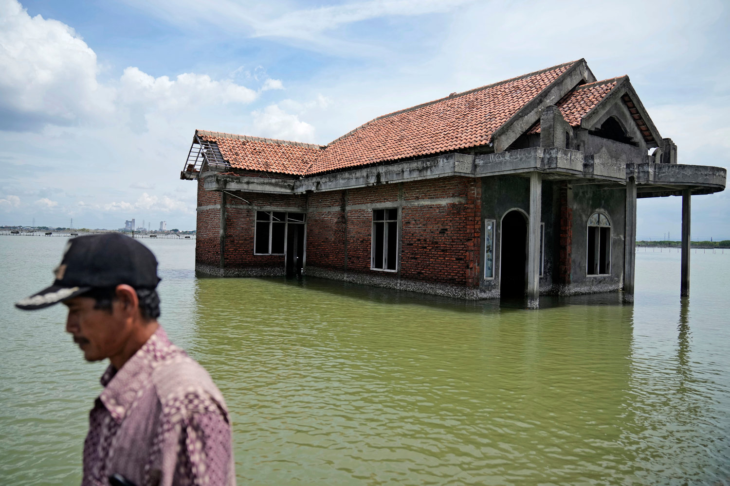 A man walks past a house abandoned after it was inundated by water due to the rising sea level in Sidogemah, Central Java, Indonesia, Nov. 8, 2021. Climate hazards such as flooding, heat waves and drought have worsened more than half of the hundreds of known infectious diseases in people, such as malaria, hantavirus, cholera and even anthrax, according to a new study released Monday, Aug. 8, 2022.