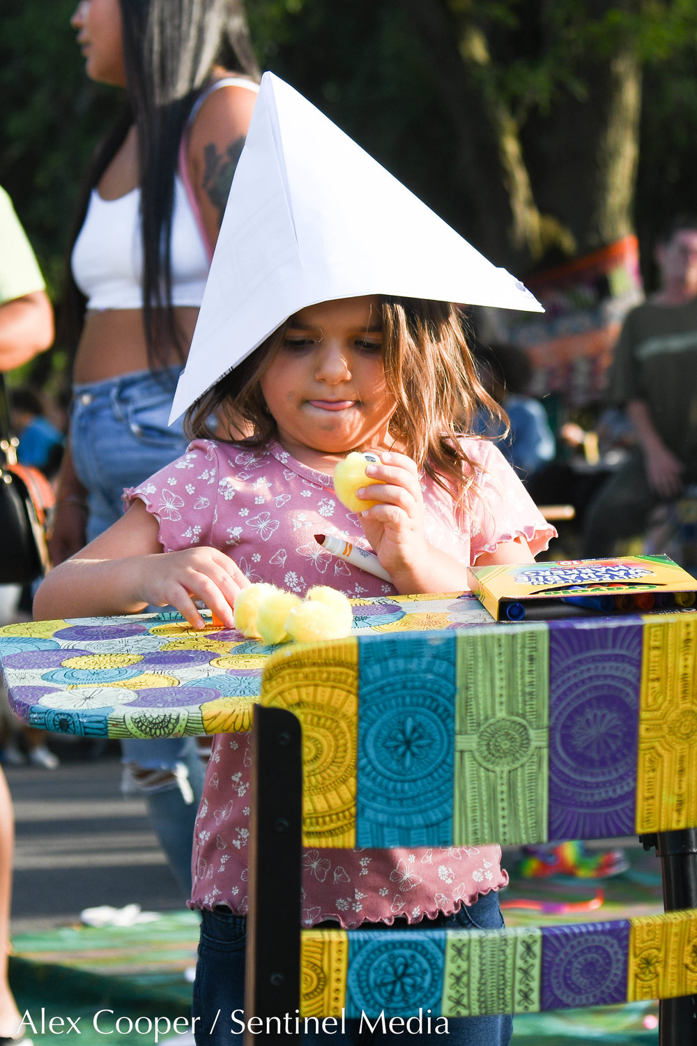 A young girl makes a paper hat out of crafts during the Levitt AMP Utica concert series on Monday at Kopernik Park.