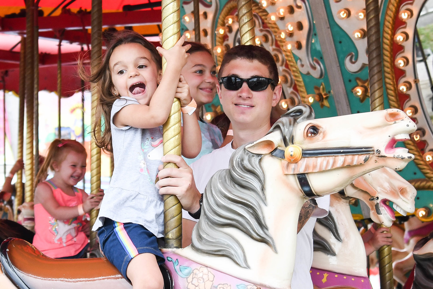 From left, Ellie Durr and her sister Evelyn Durr ride the carousel with their dad Joe Durr on Thursday at the Herkimer County Fair.