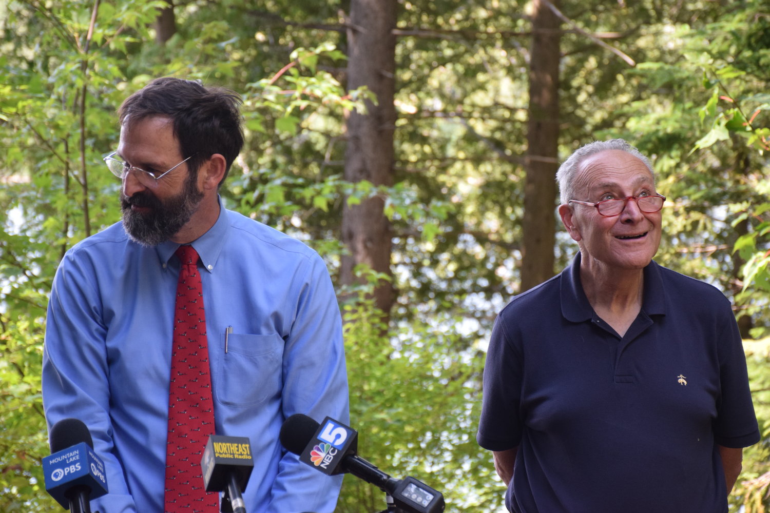 Adirondack Council Executive Director Willie Janeway, left, discusses the Inflation Reduction Act of 2022 as U.S. Sen. Chuck Schumer smiles at a hawk in the treetops at Heart Lake in Lake Placid on Monday.  (AP Photo/Adirondack Daily Enterprise)