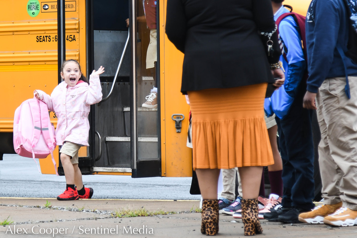 A young girl waves to faculty members while getting off the bus during the first day back to school at Utica Academy of Science Elementary School on Tuesday in Frankfort.