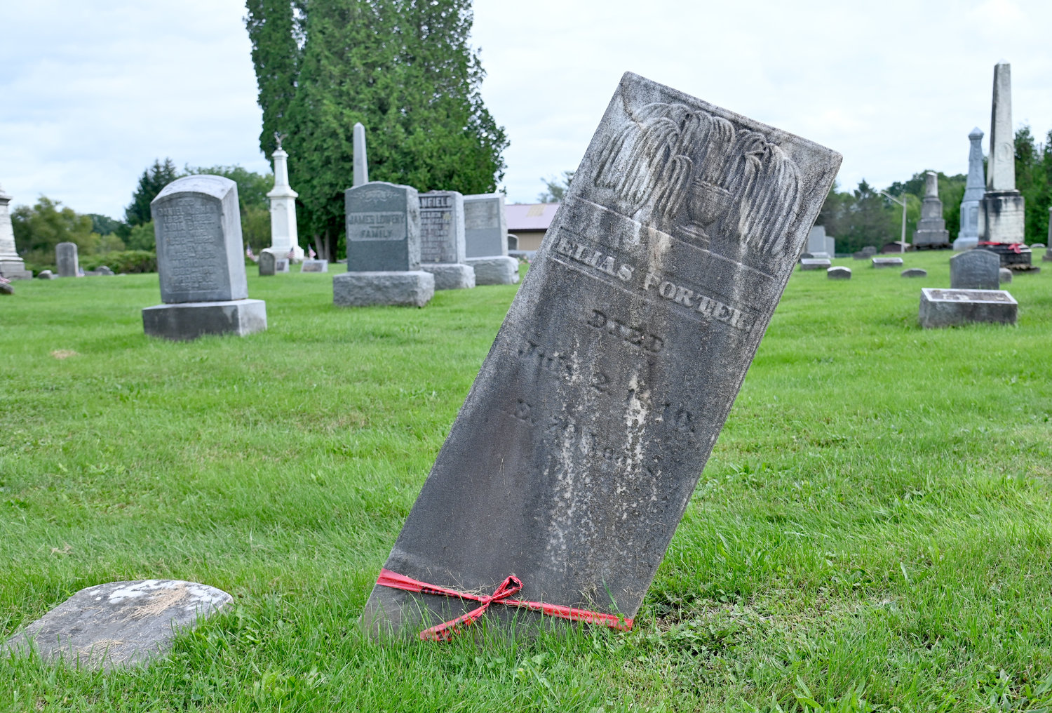 A red ribbon is tied around a tilted headstone at the Oriskany Cemetery off Cider Street on Wednesday. A $72,765 grant will help fix this and other headstones and monuments at the cemetery, officials said.