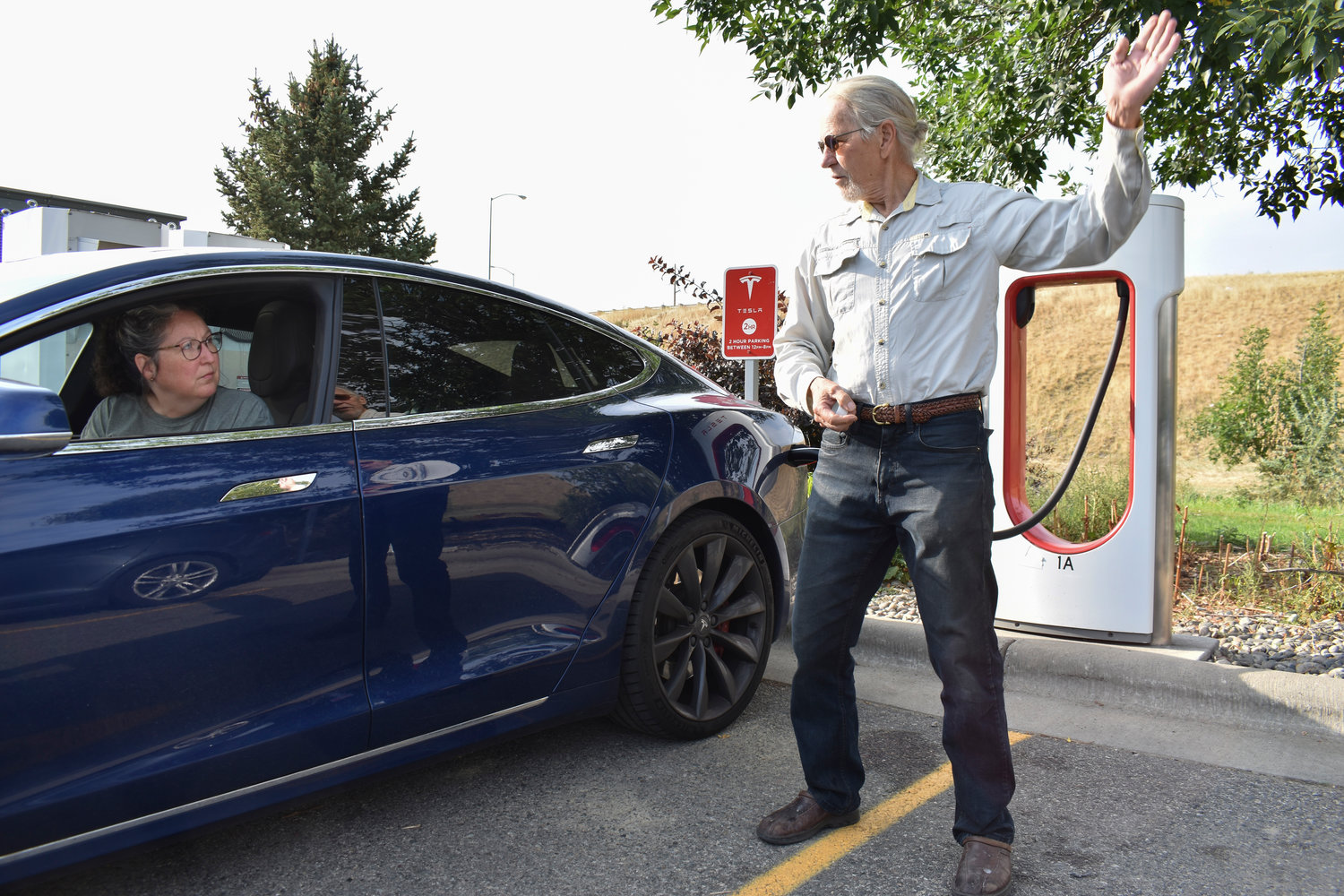 Jeannette Englehart of Billings, Mont. speaks with fellow electric vehicle owner Bob Palrud of Spokane, Wash. as they charge their cars at a station near Interstate 90, on Wednesday Sept. 14, 2022, in Billings, Mont. Englehart said there are not many charging stations in rural areas of Montana and she primarily uses the vehicle for local trips. (AP Photo/Matthew Brown)