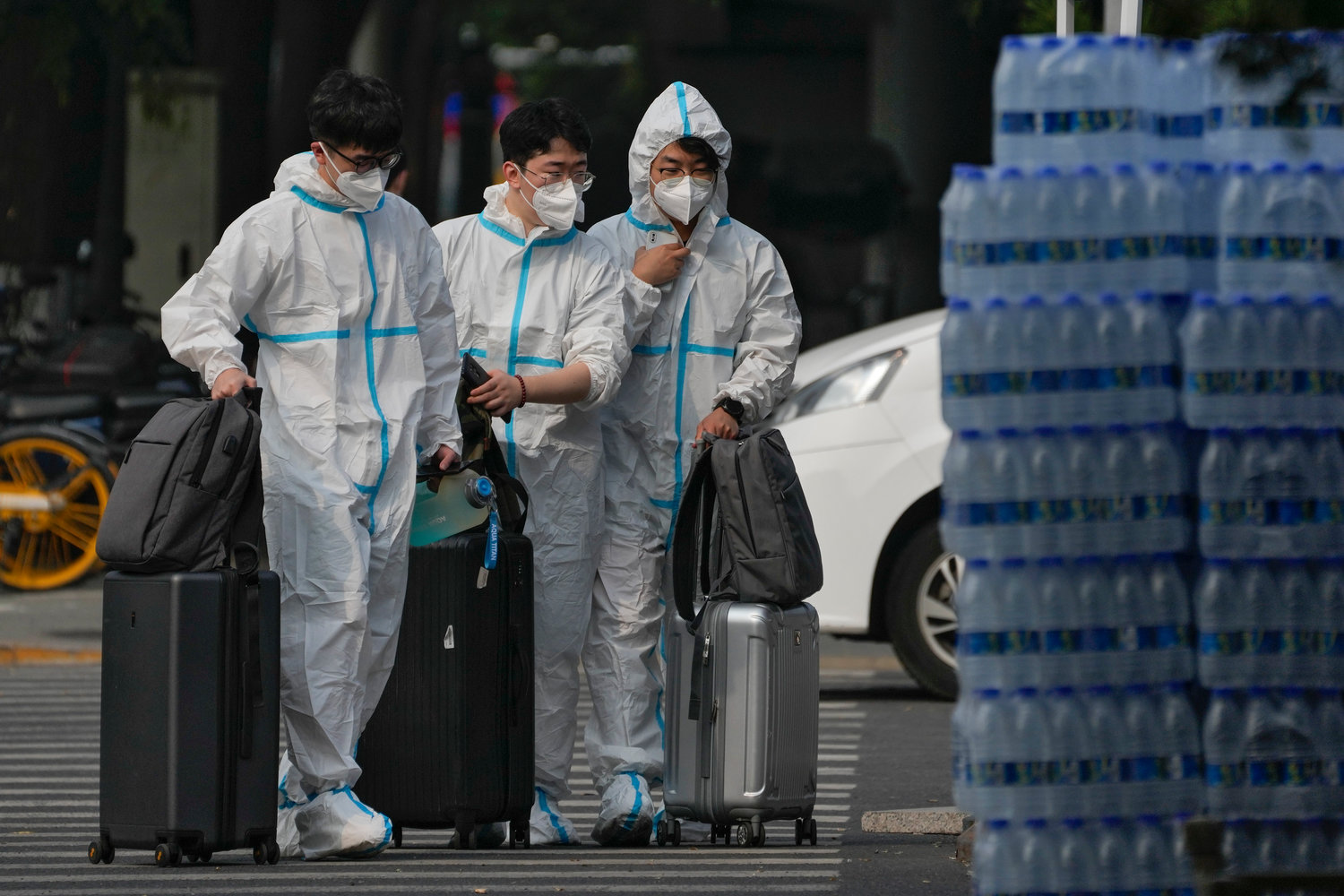 People wearing protective suits with their luggage enter the shuttered Communication University of China in Beijing, Monday, Sept. 12, 2022. Hundreds students at China's premier college for broadcast journalists have been sent to a quarantine center after a handful of COVID-19 cases were detected in their dormitory. (AP Photo/Andy Wong)