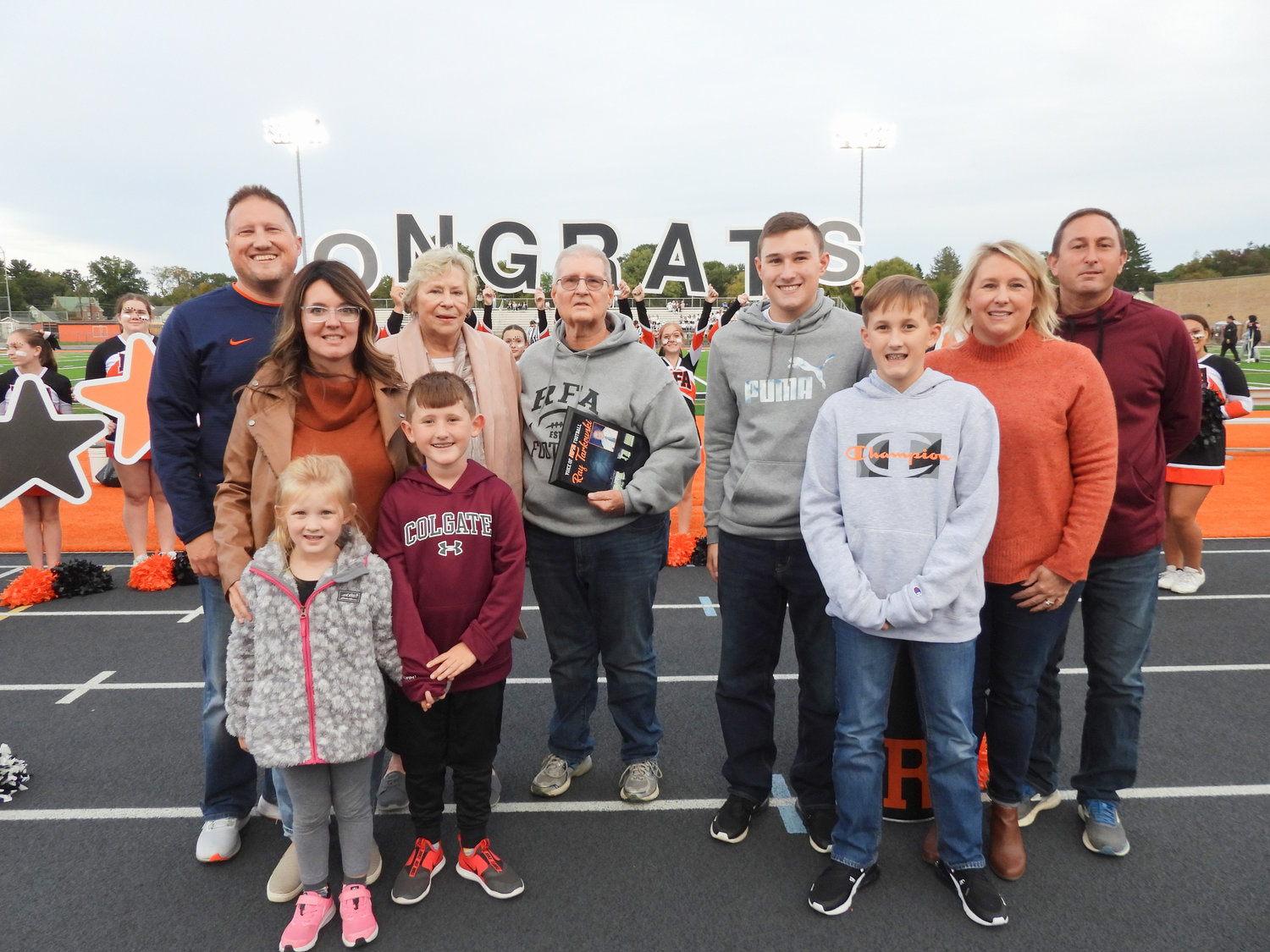 Raymond Tarkowski poses with his family, with his plaque in hand, before Friday's Rome Free Academy football game at RFA Stadium. The voice of the RFA football team was honored for his 49 years at the microphone when the district unveiled the press box at the stadium that is now named in his honor.