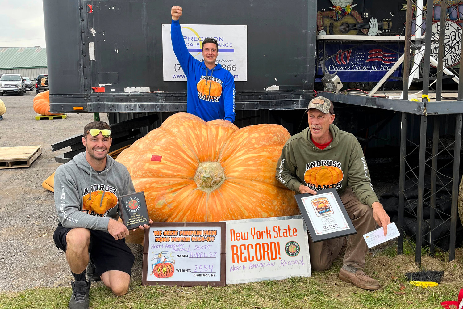 In this photo provided by The Great Pumpkin Farm, Emmett Andrusz, from left, Steve Andrusz and Scott Andrusz, pose with the record setting 2,554-pound pumpkin, in Clarence, N.Y., Saturday, Oct. 1, 2022. Scott Andrusz's entry broke the previous record of 2,528 pounds.