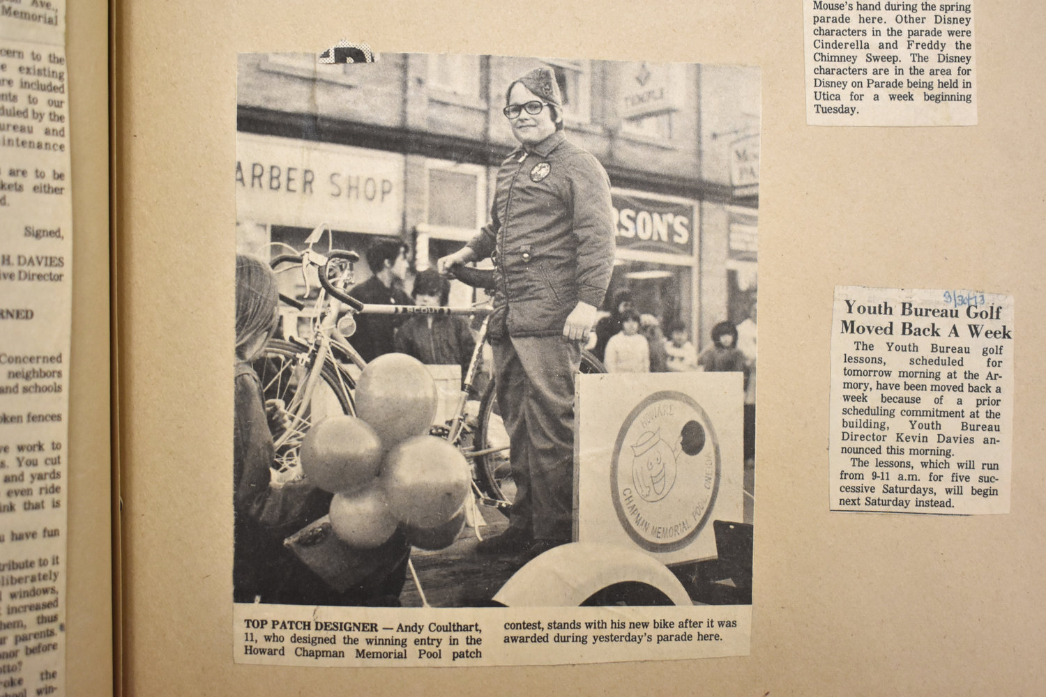 The caption from this newspaper photo from the early 70s reads: "Top patch designer -  Andy Coulthart, 11, who designed the winning entry in the Howard Chapman Memorial Pool patch contest, stands with his new bike after it was awarded during yesterday's parade here." Behind him, one can see glimpses of what downtown looked like with its variety of businesses.