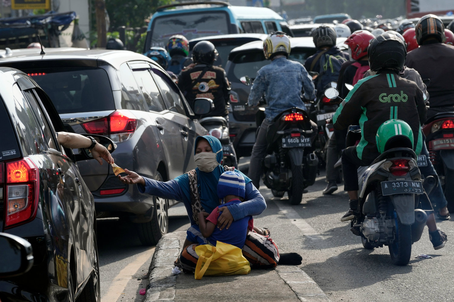 A motorist gives money to beggars while stuck in the morning rush hour traffic in Jakarta, Indonesia, Monday, Nov. 14, 2022. The 8 billionth baby on Earth is about to be born on a planet that is getting hotter. But experts in climate science and population both say the two issues aren't quite as connected as they seem. (AP Photo/Tatan Syuflana)