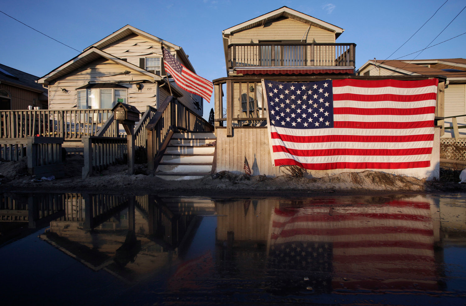 FILE - United States flags are displayed on flood-damaged homes in the Breezy Point section of Queens, N.Y., on Nov. 28, 2012. 90% of counties in the U.S. experienced a weather-related disaster between 2011-2021, according to a report published on Wednesday, Nov. 16, 2022. Over 300 million people ‚Äî 93% of the country‚Äôs population ‚Äî live in those counties. (AP Photo/Mark Lennihan, File)