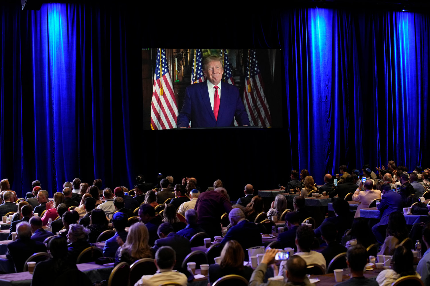FILE - People listen as former President Donald Trump speaks remotely to an annual leadership meeting of the Republican Jewish Coalition Nov. 19, 2022, in Las Vegas. Trump has spent years teasing the prospect of another presidential run. But in the first week since announcing his third bid for the White House, he's done little to suggest that he's organizing a traditional campaign. (AP Photo/John Locher, File)