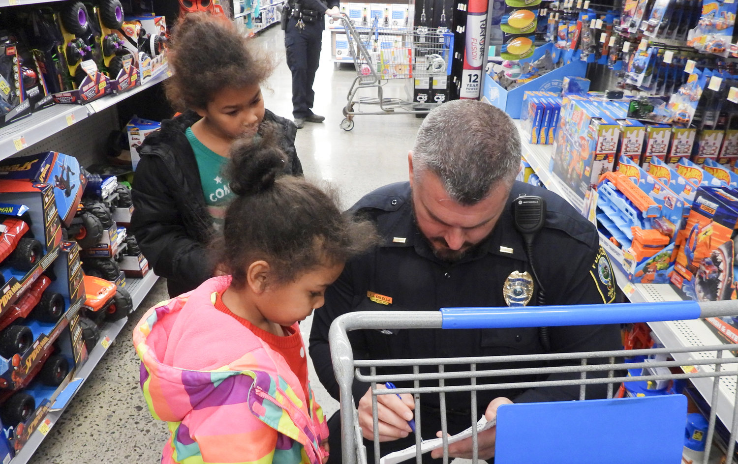 Lieutenant Matt Colella checks over the list of five-year-old Natalia Wallace — in pink — at the Oneida Police Department's Shop with a Cop event on Saturday, Dec. 10, while seven-year-old Tatiana Irvin looks on. Around 86 children were brought into Walmart on Saturday for a shopping spree with a $100 budget.