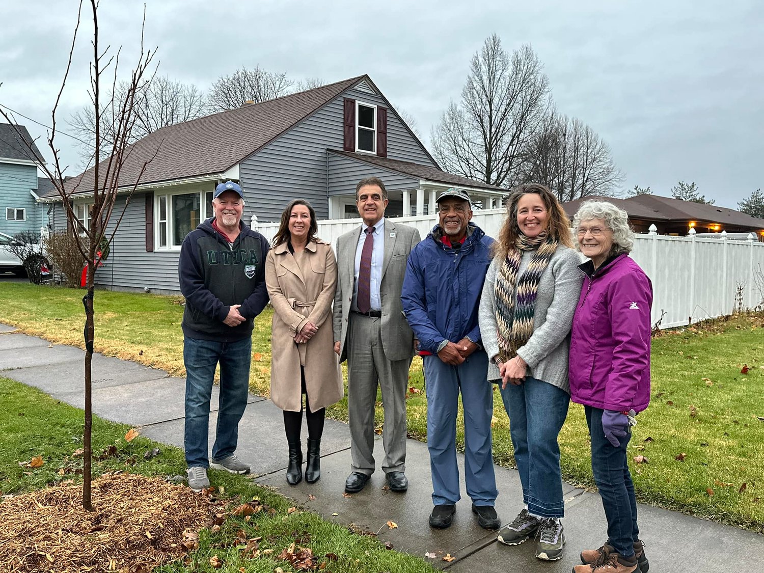Jerry Kraus and Tina Pavlot from the Rotary Club of Utica, Utica Mayor Rob Palmieri, David Jones from the Rotary Club of Utica, homeowner Lynne Morinitti and Barbara Freeman from the Unitarian Universalist Church’s Climate Action Team stand alongside a blossoming cherry tree.