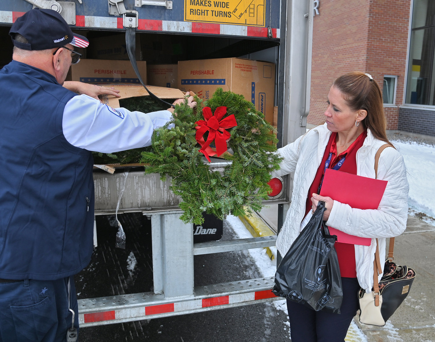 Danielle Sexton, general transportation manager at the Walmart Distribution Center in Marcy, right, checks out a wreath from Walmart driver Art Moule after the truck arrived full of wreaths on Monday, Dec. 12, at Notre Dame Jr.-Sr. High School in Utica.