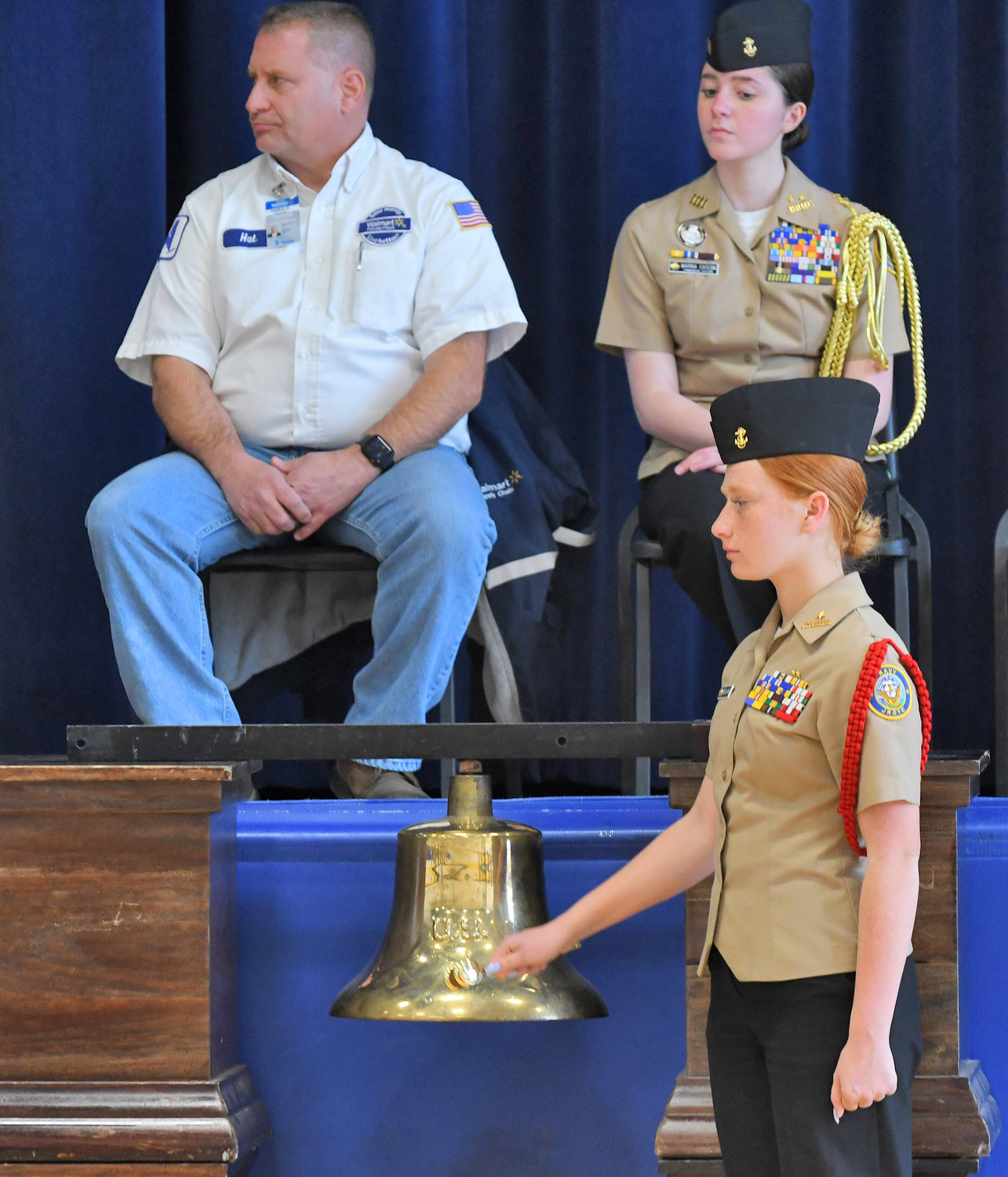 Notre Dame Navy Junior ROTC Cadet Paige Trevisani rings the bell Monday, Dec. 12 during the Wreaths Across America ceremony at the high school. In the background is Walmart truck driver and veteran Hal Coleatas, left, and NJROTC Commanding Officer Marina Cascini.