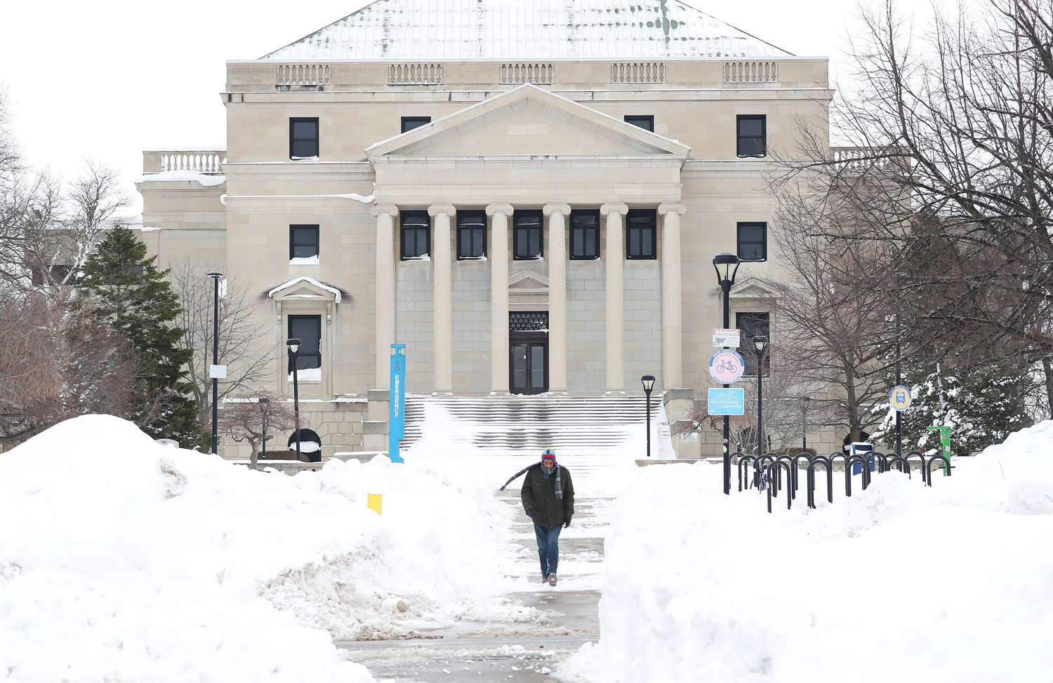 Gerald Crosby walks down a sidewalk surrounded by snow on University at Buffalo campus in Buffalo, N.Y., on Tuesday, Dec. 27, 2022. This comes days after a blizzard hit four Western New York counties. (Joseph Cooke/The Buffalo News via AP)