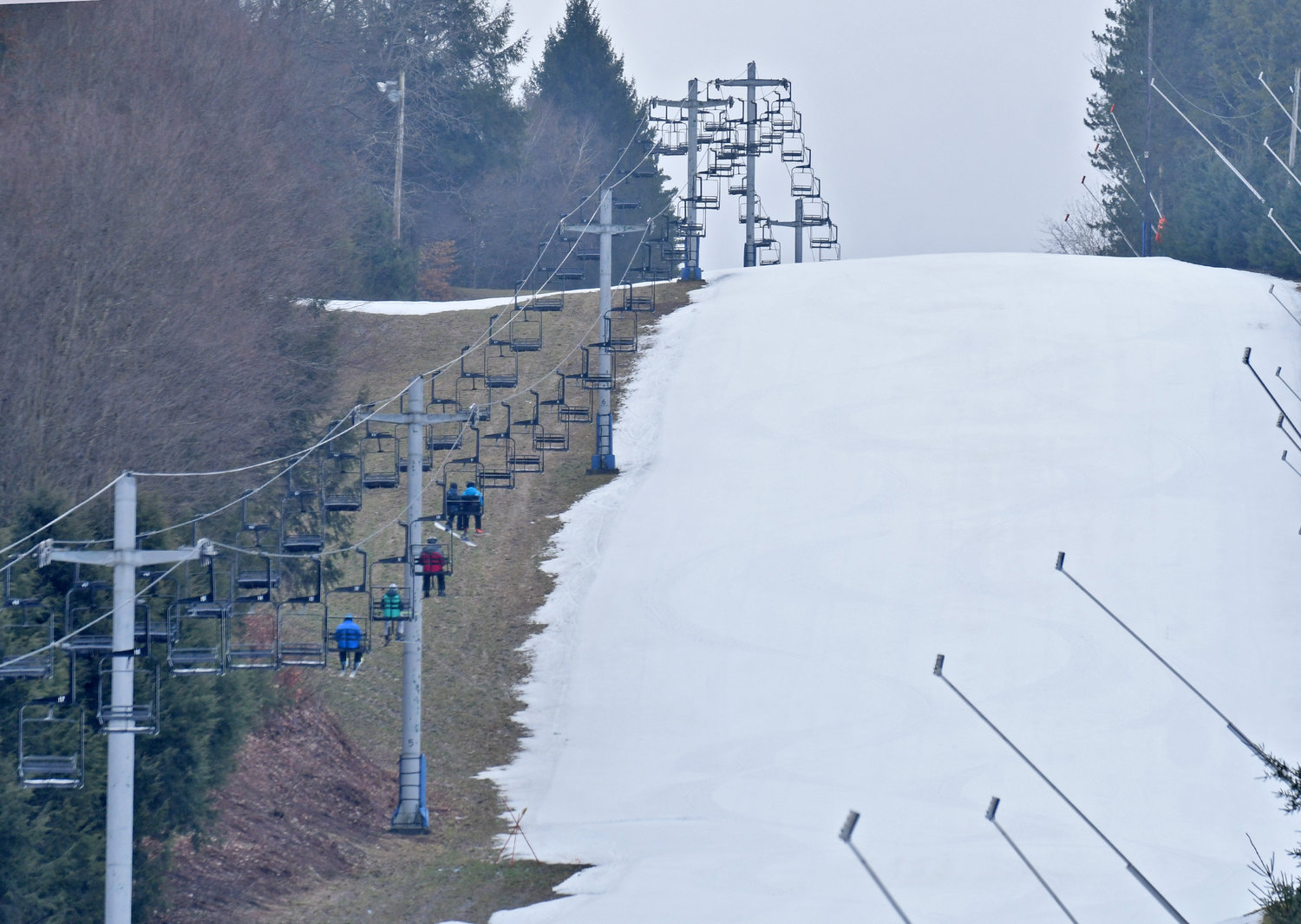 Skiers ride a lift up at Woods Valley next to the "Copy Cat" run on Friday, January 6, 2023. Warmer weather conditions leave the trails surrounded by grass.