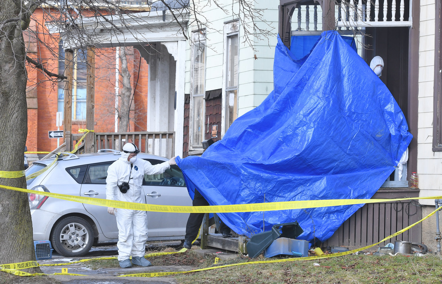 Investigators dressed in protective suits examine the scene after a man was found dead on this porch on Eagle Street in Utica early Wednesday morning. Utica Police said one person is in custody in connection to the suspected homicide.