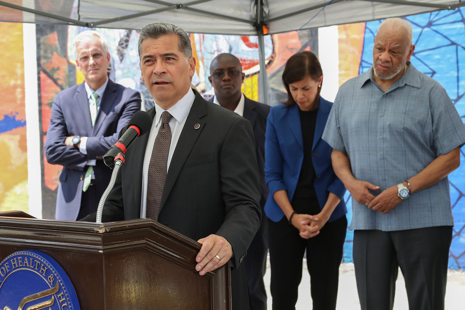Xavier Becerra, Secretary of the Department of Health and Human Services, speaks at the podium during a press conference on the kickoff of 988, a new national mental health hotline, in West Philadelphia, July 15, 2022. The press conference took place in front of the Contemplation, Clarity and Resilience mural by artist Eric Okdeh, which is a mural that represents, among many other things, the process of overcoming hardships.