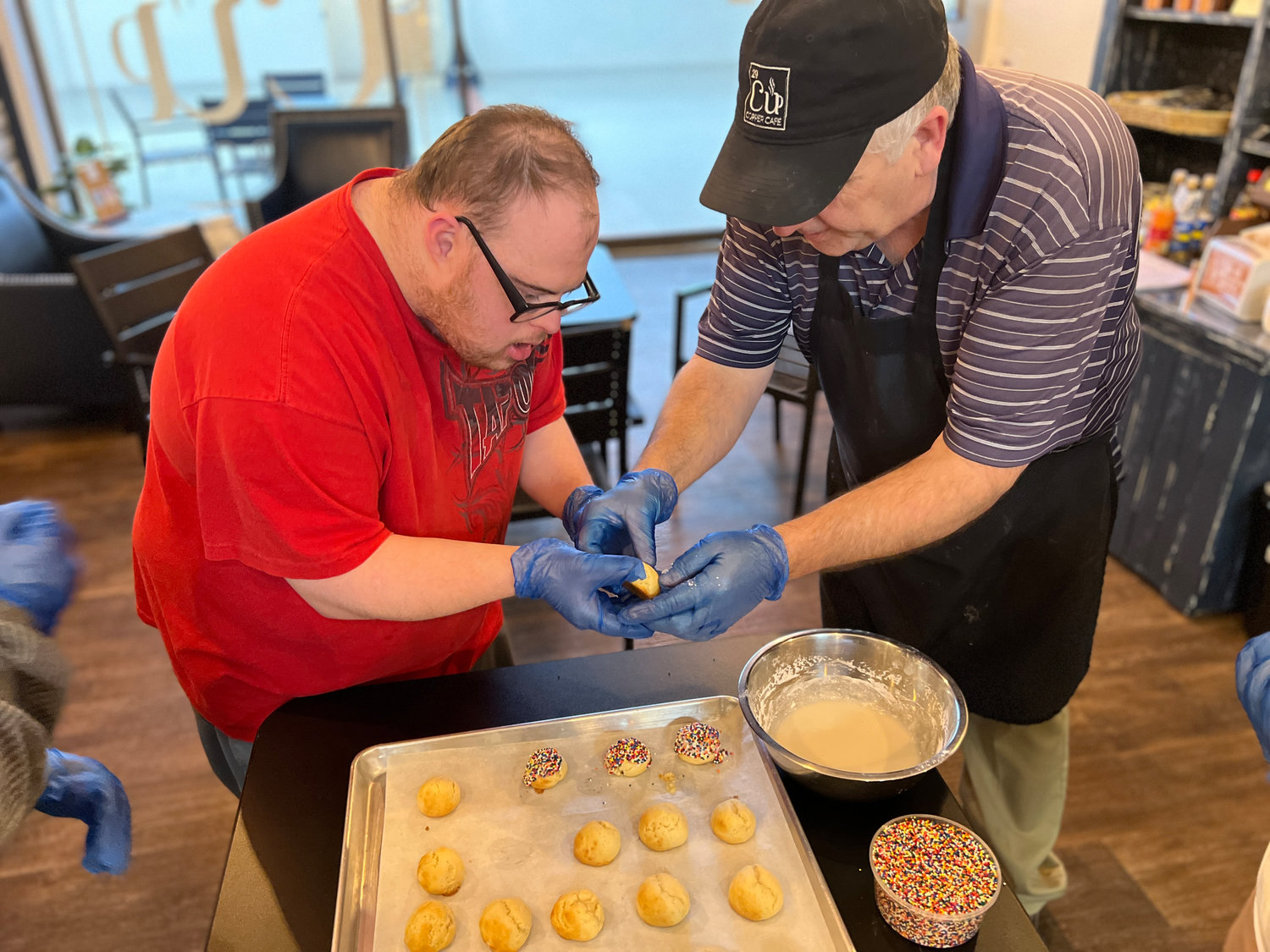 Copper Café Head Chef Eric Kennedy teaches pre-vocational participant James Michael Kent how to frost ricotta cookies in a baking class, sponsored by the Bonacci family recently. The program, in honor of the late Augustina “Gussie” Brindisi, helps individuals with disabilities learn a variety of life and employment skills.