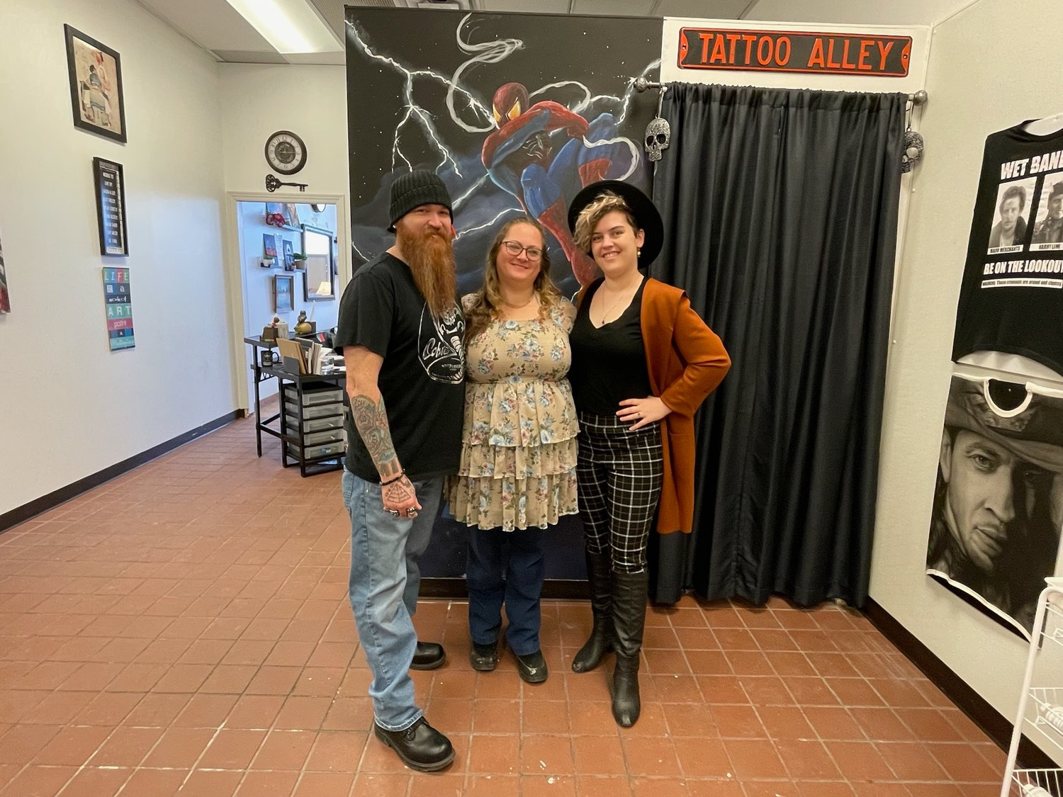Art Instructor Steve Snegon, Administrative Director Moria Egan, and Assistant Instructor Caitlin Carlo, stand inside E-98 Art Studio & Gallery on Rome-Taberg Road, in front of a Spiderman mural painted by Steve.
