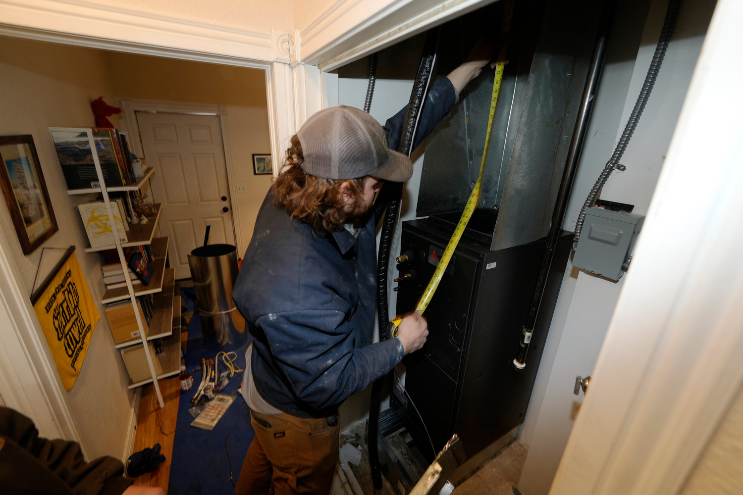 John Paul uses a tape measure during the installation of a heat pump in an 80-year-old rowhouse Friday, Jan. 20, 2023, in northwest Denver.